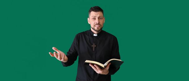 Verwirrter Priester mit Bibel auf grünem Hintergrund  - Foto, Bild
