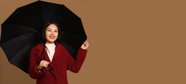 Beautiful young Asian woman with umbrella on brown background with space for text - Photo, Image