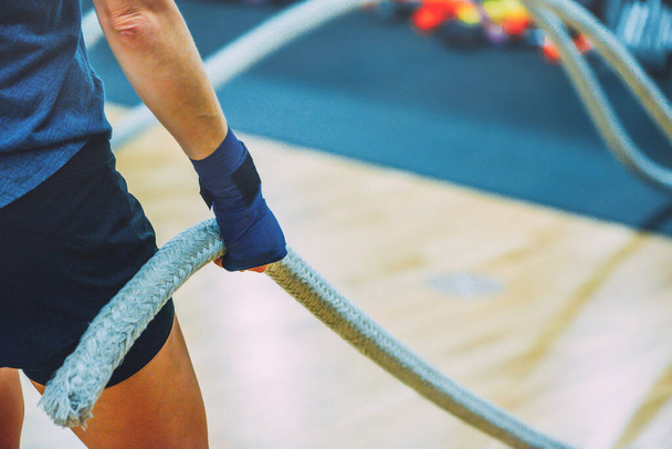 Vista lateral de una joven caucásica dedicada haciendo ejercicio con cuerdas de batalla en el club de salud, espacio para copiar. - Foto, imagen