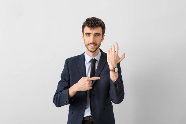 Mladý podnikatel v obleku ukazuje na náramkové hodinky na světlém pozadí - Fotografie, Obrázek