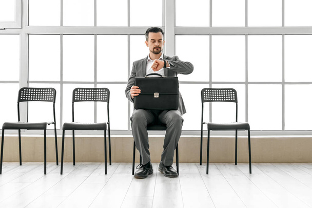 Fiatal férfi nézi karóra, miközben vár állásinterjúra az irodában - Fotó, kép