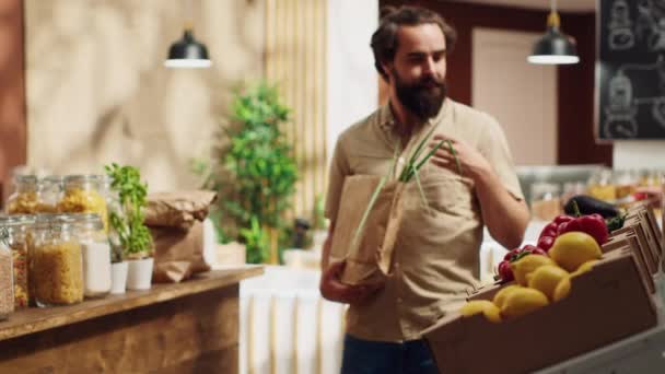 Hombre en la tienda de basura cero usando bolsa de papel, comprando verduras, sintiendo la fiebre de la dopamina mientras los huele. Cliente que experimenta felicidad probando un producto en una tienda local sin una política de plásticos de un solo uso - Imágenes, Vídeo