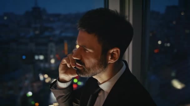 Overworked business man calling standing at office window late evening. Serious executive manager talking phone with partners discussing work at night close up. Bearded businessman speaking telephone. - Footage, Video