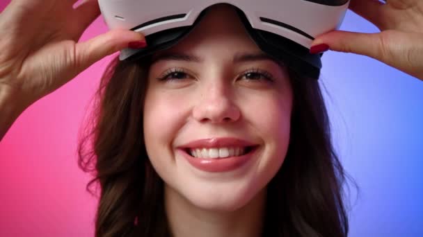 Молодая улыбающаяся женщина в спортивном костюме надевает виртуальную реальность VR гарнитуру и позирует в студии с синим и красным фоном - Кадры, видео