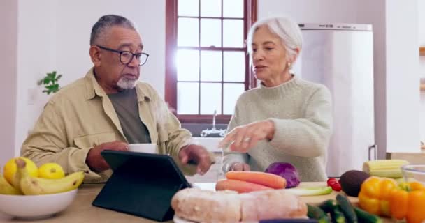 Cocinar, hablar o pareja de ancianos con tabletas o alimentos para una dieta vegana saludable juntos en la jubilación en casa. Mujer en línea, interracial o mayor en la cocina hablando con un hombre mayor para la receta de la cena. - Metraje, vídeo