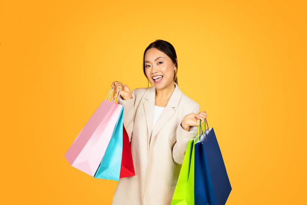 Радостная азиатская женщина тысячелетия на шоппинге, ее руки полны красочными сумками, отражающими как восторг покупок, так и современный, ориентированный на потребителя образ жизни молодых людей сегодня - Фото, изображение