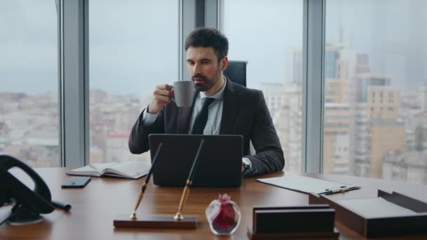 Koncentrált vezérigazgató néz laptop képernyőn iszik forró kávét a modern munkahelyen közeli. Komoly üzletember, aki üzleti terveken gondolkodik irodai íróasztal mellett. Manager létrehozása ötletek élvezi ital. - Felvétel, videó