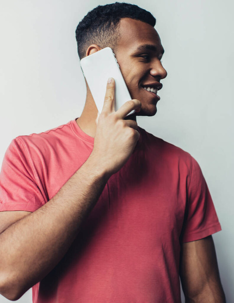 Positive black man calling to friend for communicating and discussing details while standing near promotional background, African American hipster guy using smartphone app for online talking - Фото, изображение