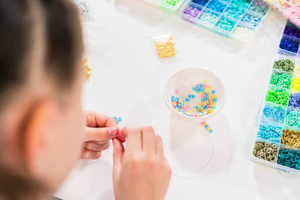 Маленька дівчинка любить створювати різнокольорові браслети з яскравим набором глиняних намистин. - Фото, зображення