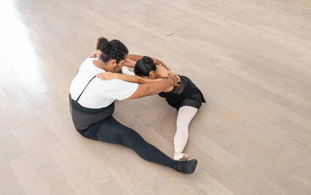 joven estudiante de ballet afroamericano estirándose con la ayuda de su instructor de bailarina hispana - Foto, Imagen