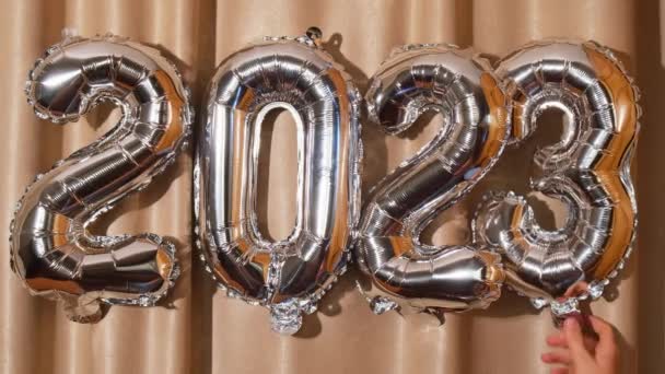 Gelukkig Nieuwjaar 2023 verander naar 2024 metalen ballonnen op atlas textiel achtergrond. Wenskaart zilveren folie ballonnen nummers Kerstvakantie concept. Feestfeest felicitatie decoratie - Video