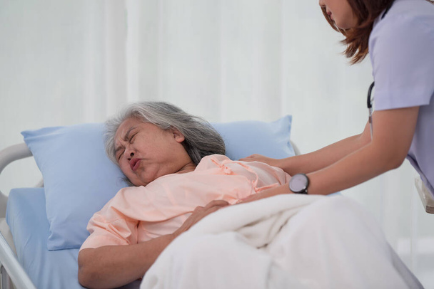 Azjatycka pielęgniarka pomaga starszej Azjatce z bólem brzucha na łóżku w szpitalu z diagnozą lub leczeniem, lecząc starszą kobietę - Zdjęcie, obraz