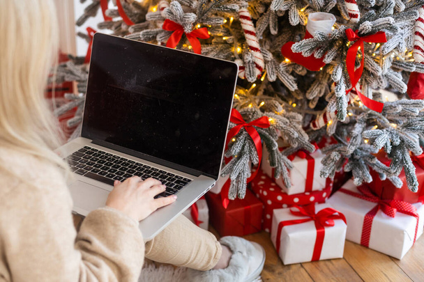 Happy young woman working on laptop in front of christmas tree - Photo, Image