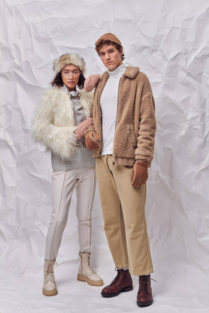 trendy interracial couple in warm faux fur jackets on white textured backdrop, winter fashion - Photo, Image