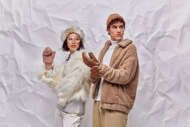 interracial couple in warm faux fur jackets looking away on white textured backdrop, winter style - Photo, Image