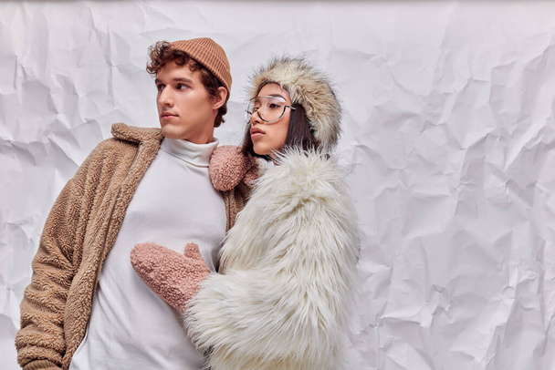 fashion lookbook concept, interracial couple in winter wear looking away on white crumpled backdrop - Photo, Image