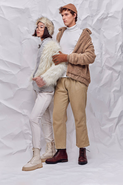 full length of multiethnic couple in worm cozy outfits looking away  on white textured backdrop - Photo, Image