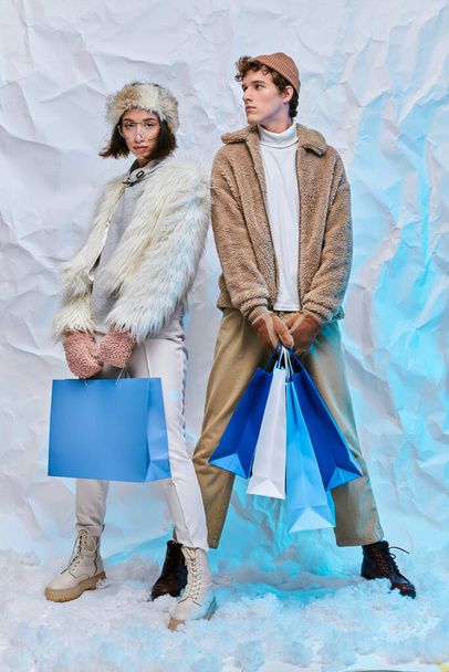 Wintershopping, interrassische Models im warmen, gemütlichen Outfit mit Einkaufstaschen im verschneiten Studio - Foto, Bild
