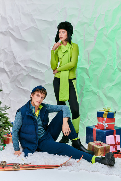 temporada festiva, pareja interracial posando en la nieve en el estudio cerca del árbol de Navidad y cajas de regalo - Foto, Imagen