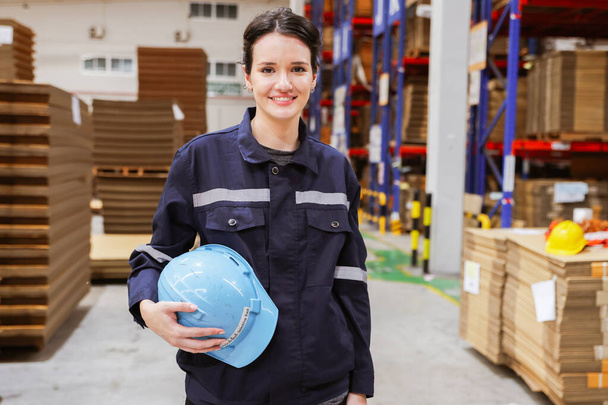 Beautiful female service professional supervisor in a cardboard box warehouse export logistics factory standing holding hardhat entering the warehouse security inspection area inside the building. - Photo, Image
