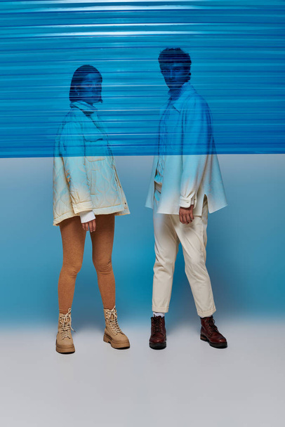 スタジオ,冬の傾向の青いプラスチック シートの背後にある革のブーツの異人種間のカップルの完全な長さ - 写真・画像