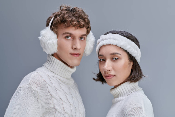 moda lookbook concept, ritratto di coppia interrazziale in abito invernale guardando la fotocamera sul grigio - Foto, immagini
