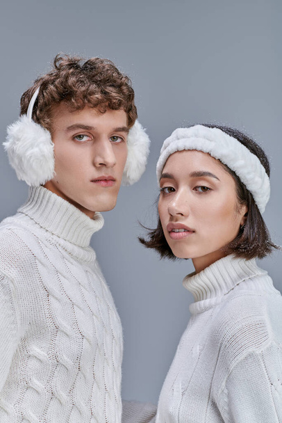winter fashion concept, portrait of multiethnic couple in warm outfit looking at camera on grey - Photo, Image