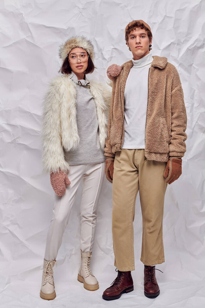longitud completa de la pareja multiétnica en ropa acogedora posando sobre fondo de textura blanca, moda de invierno - Foto, Imagen