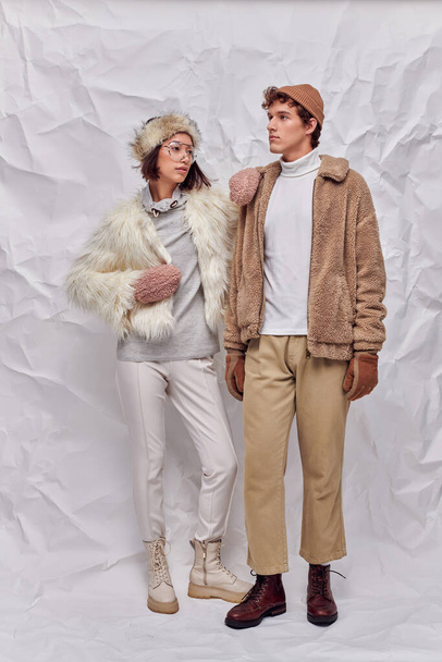 mladý mezirasový pár ve stylové zimní oblečení na bílém texturovaném pozadí, městská móda - Fotografie, Obrázek