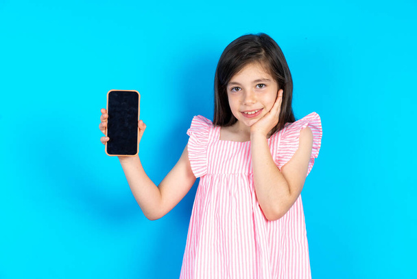 kid hold hand modern technology use touch face palm astonished impressed scream wow omg unbelievable unexpected. Beautiful caucasian little girl posing over blue studio background - Photo, Image