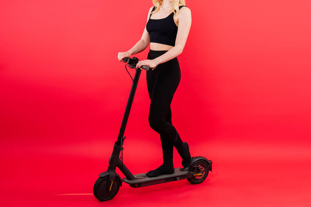 Blonde woman on a red and white background sit and stand with electro scooter and resting - Photo, Image