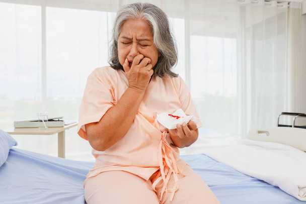 Starsza Azjatka zestresowana, płacze martwiąc się siedząc na łóżku szpitalny pogotowie cierpiące na zapalenie płuc kaszel, który naraził ją na ryzyko raka płuc był zszokowany widząc krew w plwocinie. - Zdjęcie, obraz