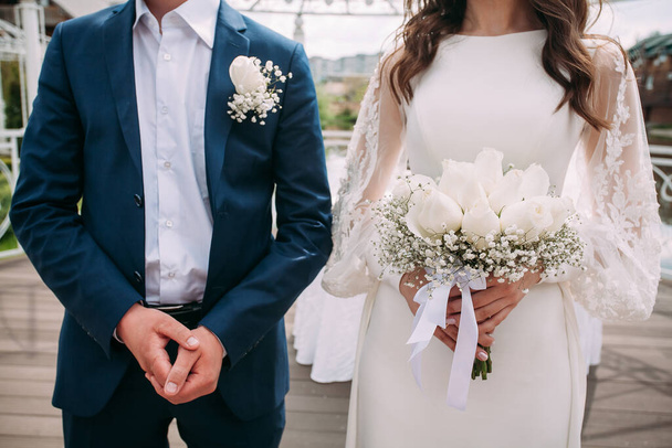 Lo sposo in abito blu e la sposa in abito bianco con un bouquet in mano. Composizione di nozze per il vostro disegno o illustrazioni creative. - Foto, immagini