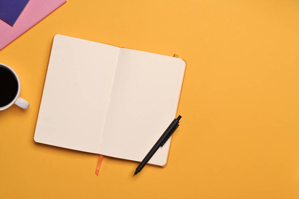 Cuaderno abierto en blanco, bolígrafo y taza de café sobre fondo amarillo. Vista superior con espacio para texto. - Foto, Imagen