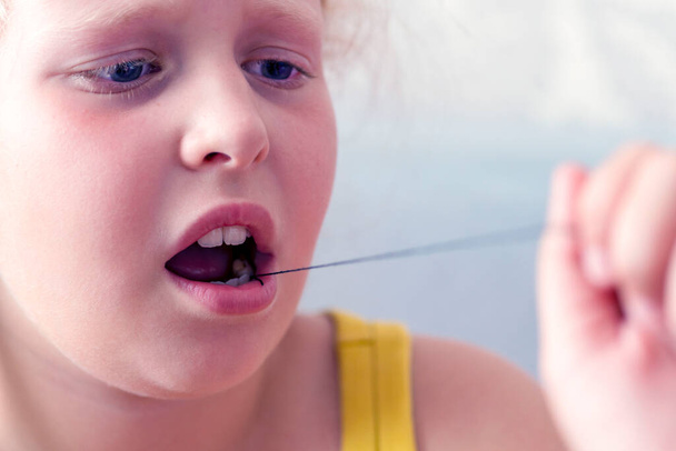女の子は,ミルクの歯を引き出すために糸を持っています. 子供の歯の除去について. 子供のミルク歯の概念喪失. 子供のための歯科ケア.歯磨きコンセプト,歯科の問題 - 写真・画像