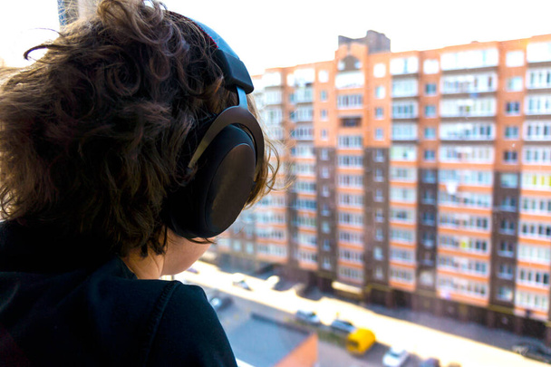 Κορίτσι με ακουστικά που κοιτάει έξω από το παράθυρο. Τα ακουστικά κλείνουν. ακουστικά δίπλα στο παράθυρο - Φωτογραφία, εικόνα