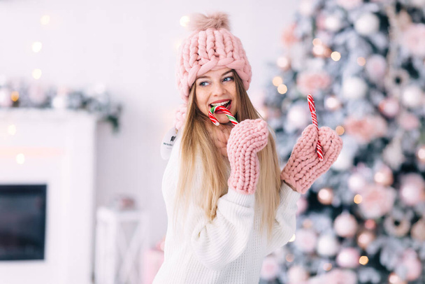 Jonge vrouw in gebreide kleding eet kerstsnoep. Kerstboom thuis. close-up. - Foto, afbeelding