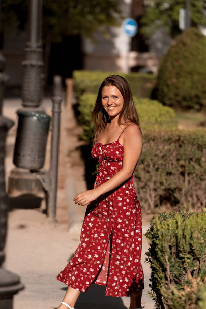 Fröhliche Frau, die im Sonnenlicht lächelt, während sie es genießt, in einem Park im Freien zu spazieren. - Foto, Bild