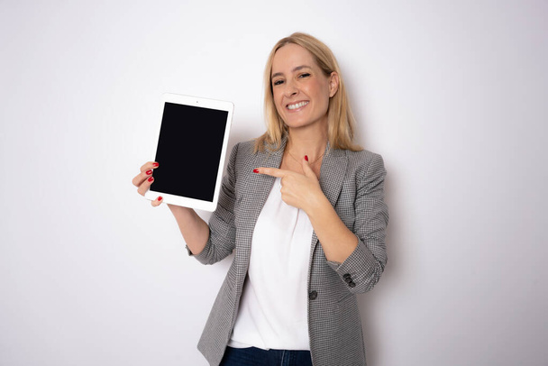 Портрет щасливої молодої блондинки з використанням планшета ізольовано на білому тлі. Усміхнена красива дівчина тримає цифровий планшетний комп'ютер. Сучасні технології та бізнес - Фото, зображення