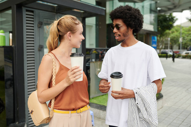 Jeunes collègues positifs debout dans la rue, buvant du café et discutant des nouvelles - Photo, image