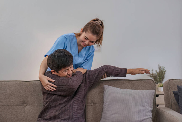 Krankenschwester unterstützt Mann bei Erholung und physikalischer Therapie, ein Senior ruht sich im Wohnzimmer aus und zeigt Freundlichkeit, während er den Gesundheitszustand eines Rentners zu Hause überprüft. - Foto, Bild
