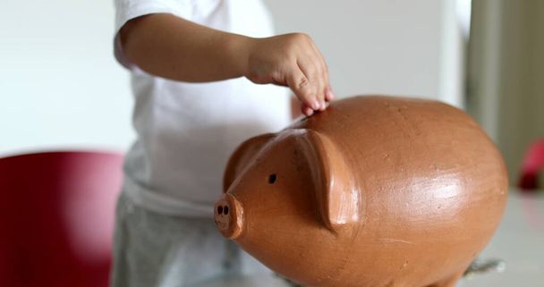 Baby hands putting coins inside piggy bank - Foto, afbeelding