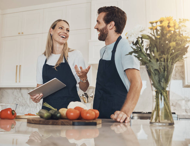 Cooking, talking or happy couple with tablet or food for a healthy vegan diet together at home. Smile, vegetables or woman speaking in kitchen with love or man learning a dinner recipe on online blog. - Photo, Image