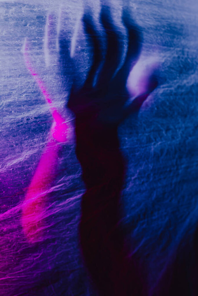 Χέρι γυναίκας που πιέζει την κουρτίνα. σιλουέτα γυναίκα πίσω από το μπλε φως θέτει μυστηριωδώς και καλλιτεχνικά - Φωτογραφία, εικόνα