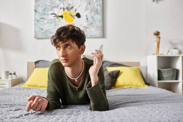 niezadowolony kręcone transseksualista osoba w casual strój rozmowy na smartfonie w sypialni, telefon - Zdjęcie, obraz