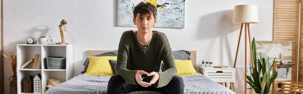 pancarta de joven transexual en traje casual mirando a la cámara y sentado en la cama en casa - Foto, imagen