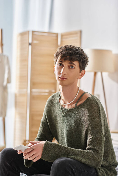 fiatal transznemű személy alkalmi öltözékben néz kamera és ül a modern lakásban - Fotó, kép