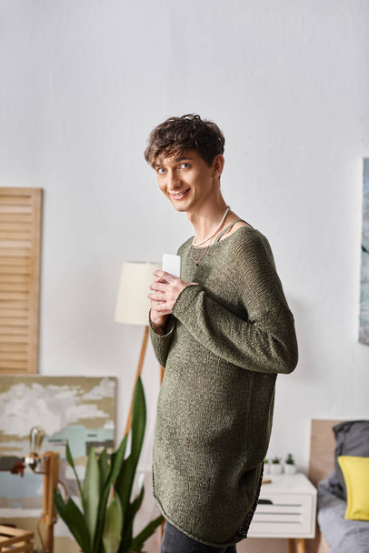 joyful curly transgender blogger using smartphone and standing in bedroom, social media influencer - Fotografie, Obrázek
