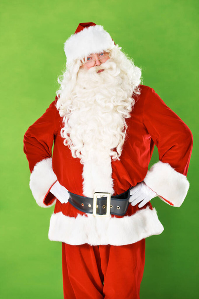 Kerstman, handen en heupen in studio portret voor kerstvakantie, feestdagen of waarschuwing. Mannelijke persoon, kostuum pak en arm gebaar op groene achtergrond voor vakantie, feest of cadeau geven. - Foto, afbeelding
