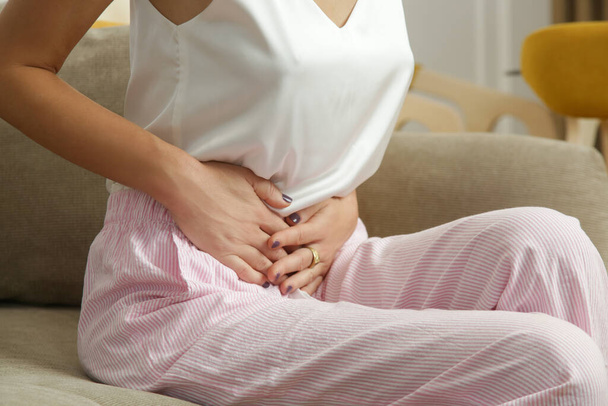 Dolor de estómago. Mujer con malestar estomacal o calambres menstruales. Una mujer joven experimenta dolor abdominal en el apartamento.  - Foto, imagen